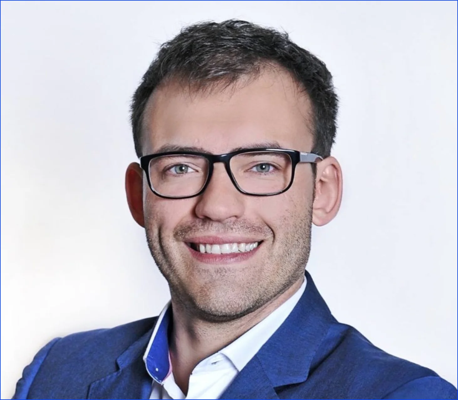 A young guy with blond hair, glasses and a bright smile