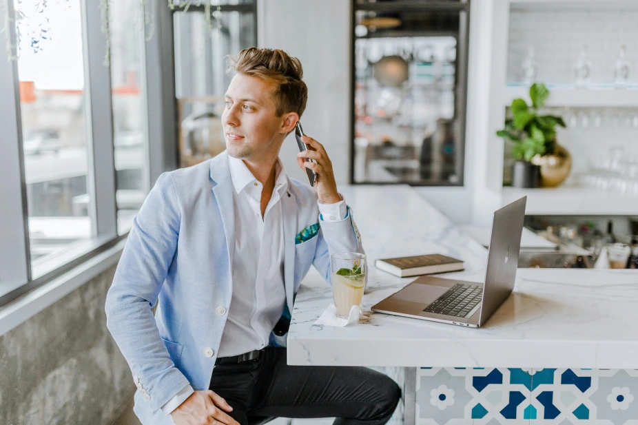 A young guy with blond hair and a blue jacket looks into the distance and talks on the phone