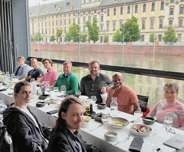 Many people are sitting at a long table behind a large window overlooking the river