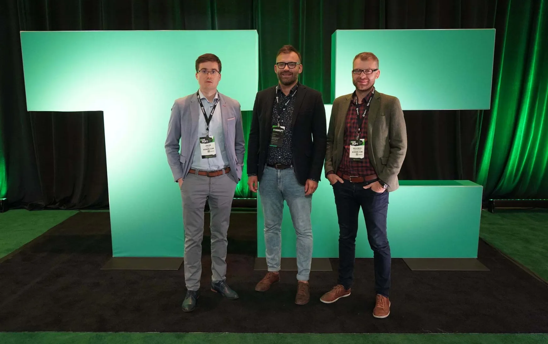 Three young guys in suits smile against a background of green neon lighting