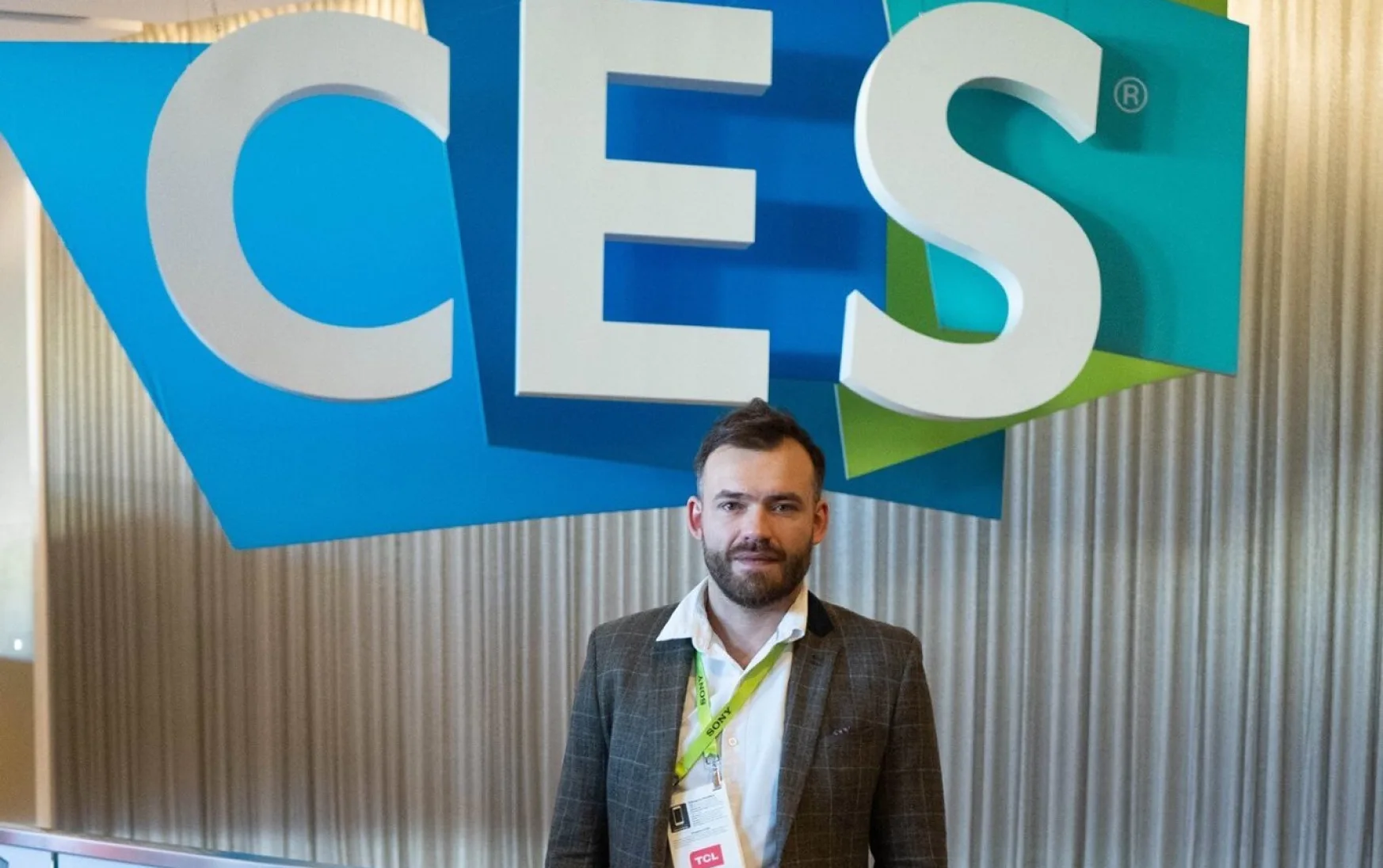 A guy in a jacket stands against the background of a large CES logo