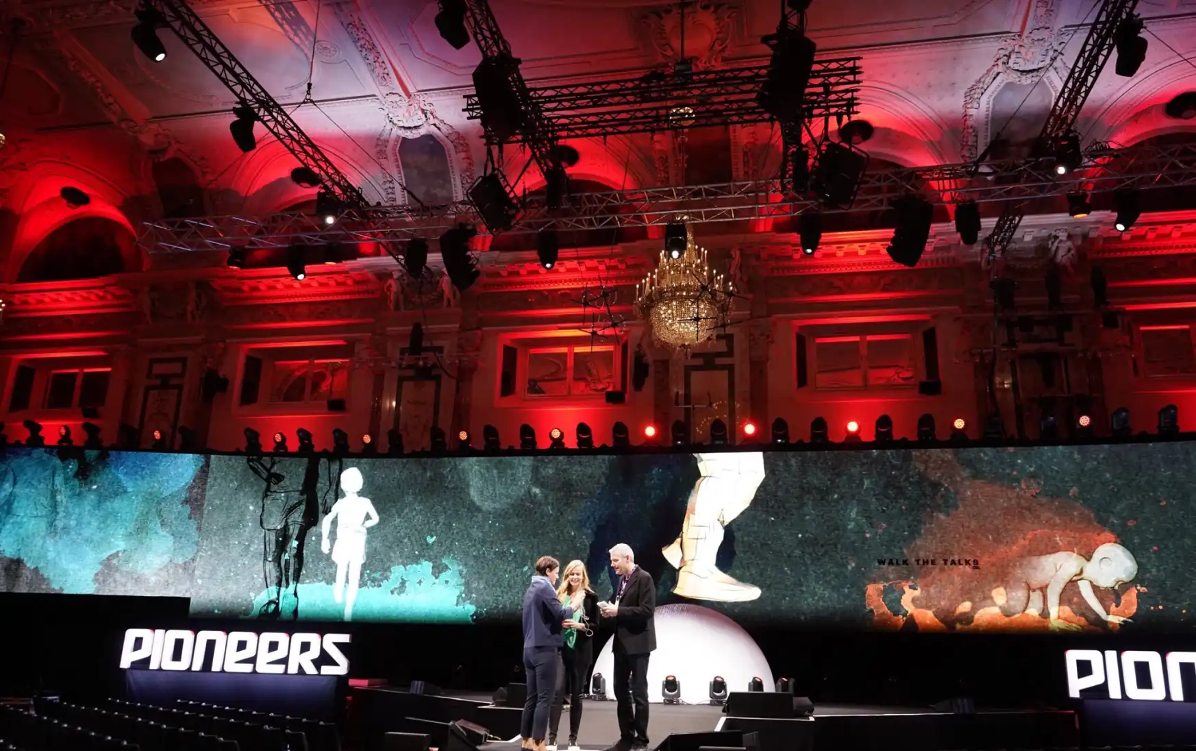 Three people on stage with a large monitor and red backlight